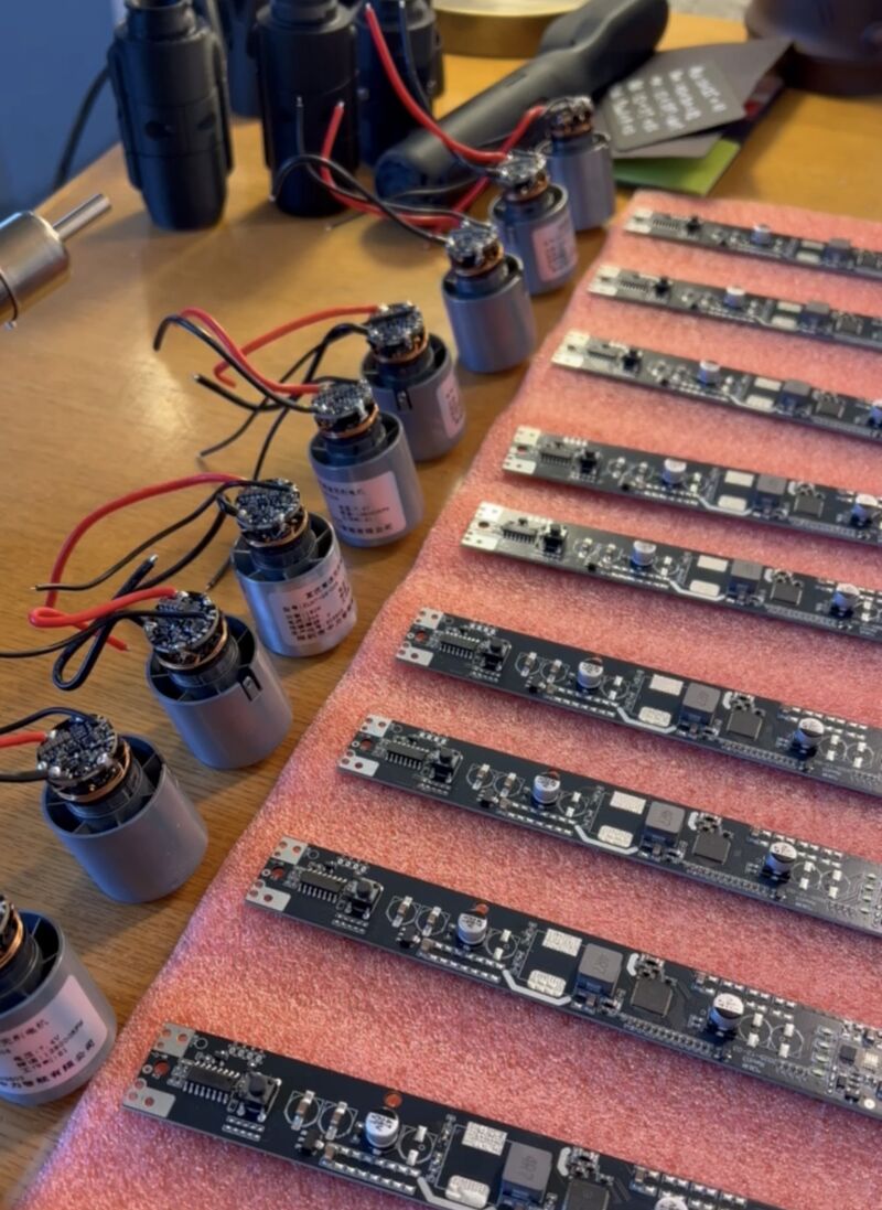 Rows of ChalkBlaster circuit boards on pink anti-static foam beside a batch of small BLDC jet-fan motors with red and black wire leads, laid out on a workbench during assembly.