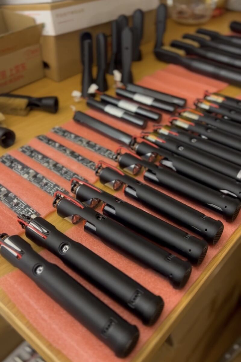 Rows of matte-black ChalkBlaster handle bodies laid out on pink anti-static foam on a workbench, part-assembled with internal wiring visible, during an in-house production batch.