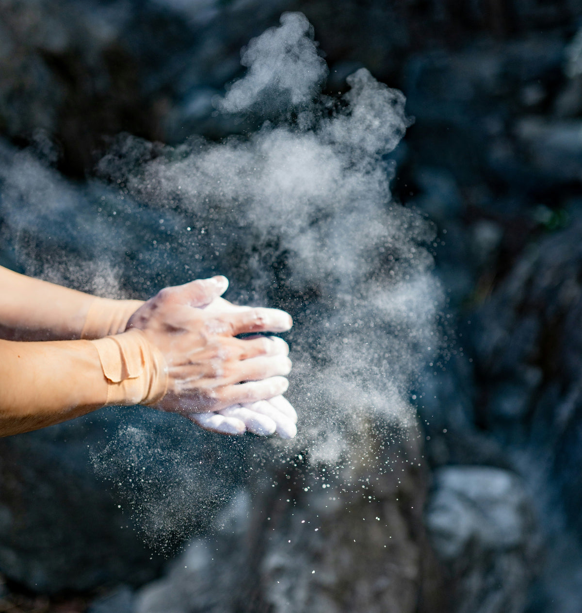 A climber clapping chalk off their hands, sending a white cloud of chalk dust into the air