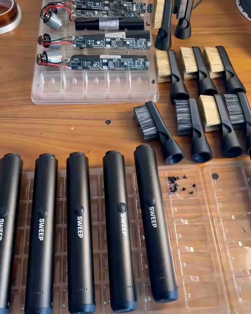 ChalkBlaster assembly bench with handles, circuit boards and batteries in trays, and finished brush heads lined up