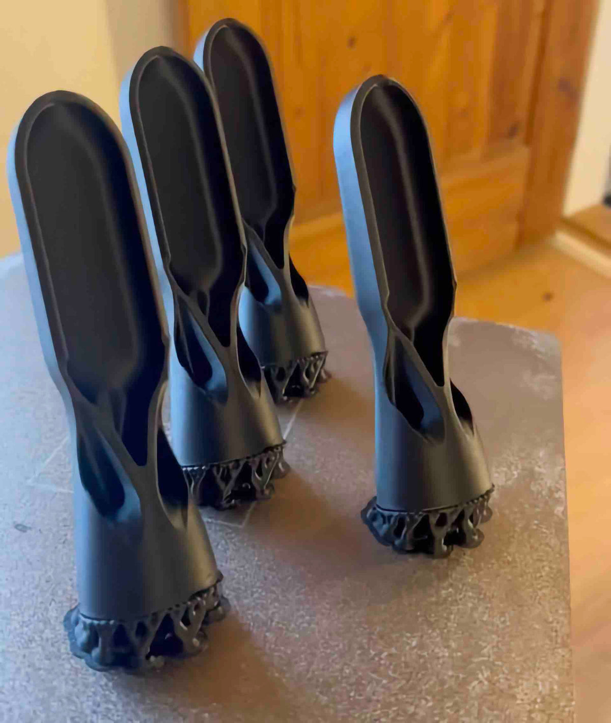 Four freshly printed ChalkBlaster brush heads standing on a print bed at an angle, with lattice supports still attached at the base