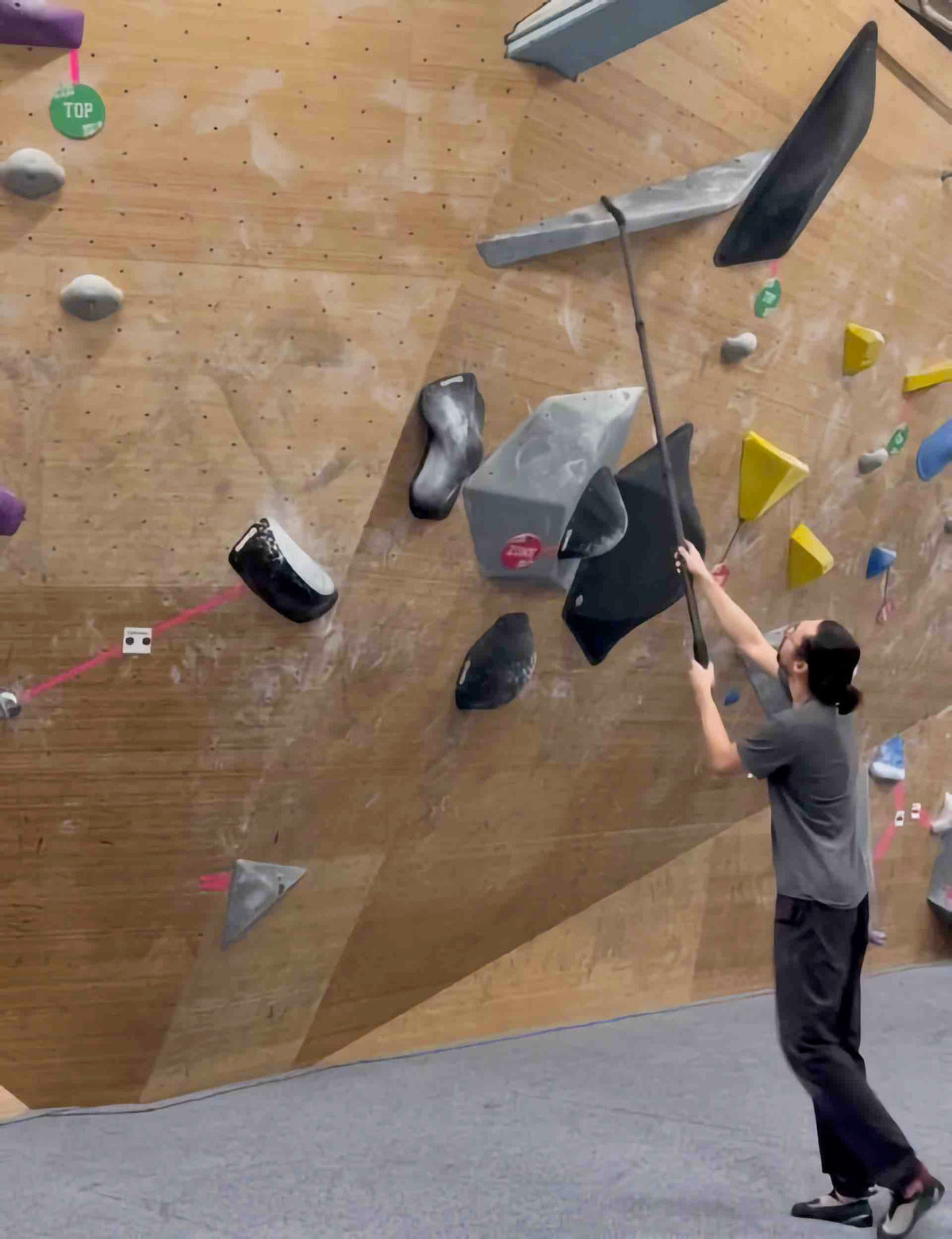 A climber cleaning high gym holds from the ground with a ChalkBlaster mounted on an extension pole