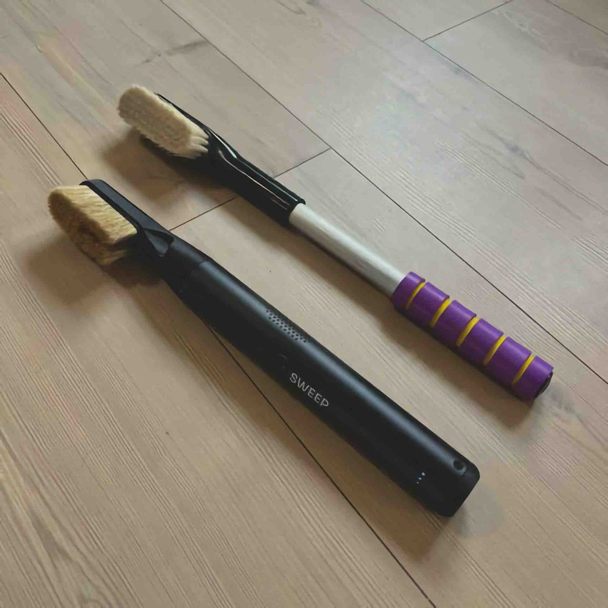 A ChalkBlaster electric brush lying next to a traditional climbing brush on a wooden floor