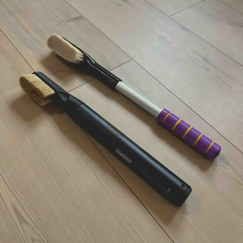 A ChalkBlaster electric brush lying next to a traditional climbing brush on a wooden floor