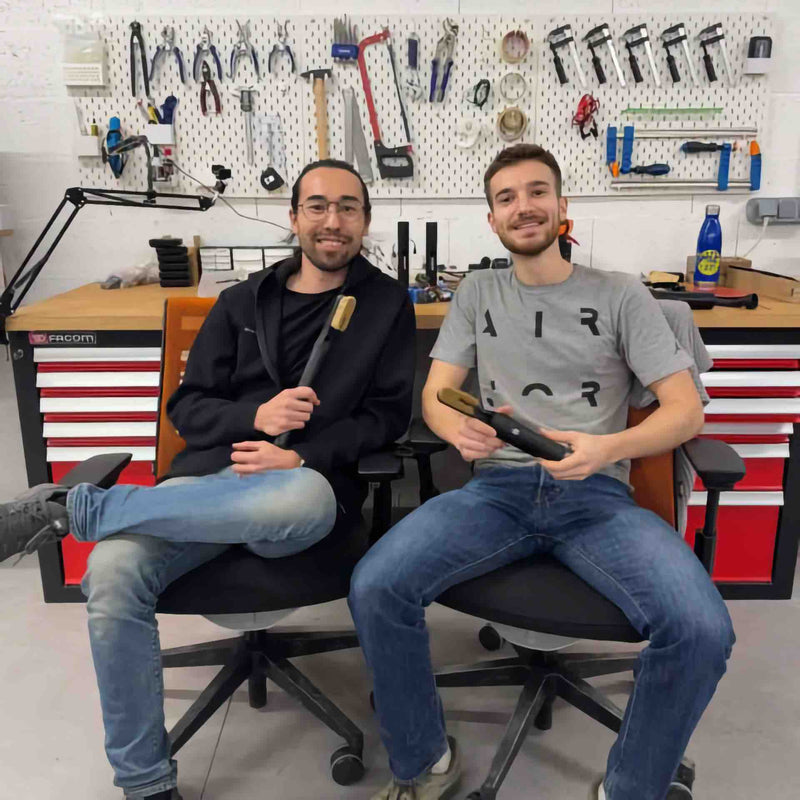 Paul and Kent, the SWEEP Climbing founders, sitting in the workshop each holding a ChalkBlaster, with a tool wall behind them
