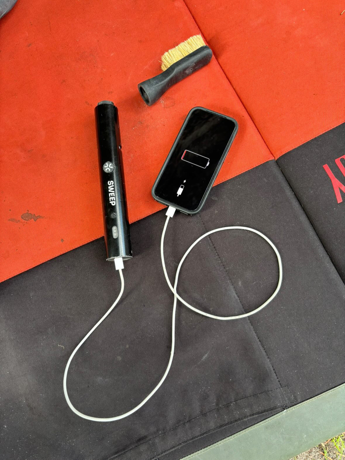 ChalkBlaster changing iphone with a usb-c cable on top of  red and black crash pad by Snap Climbing