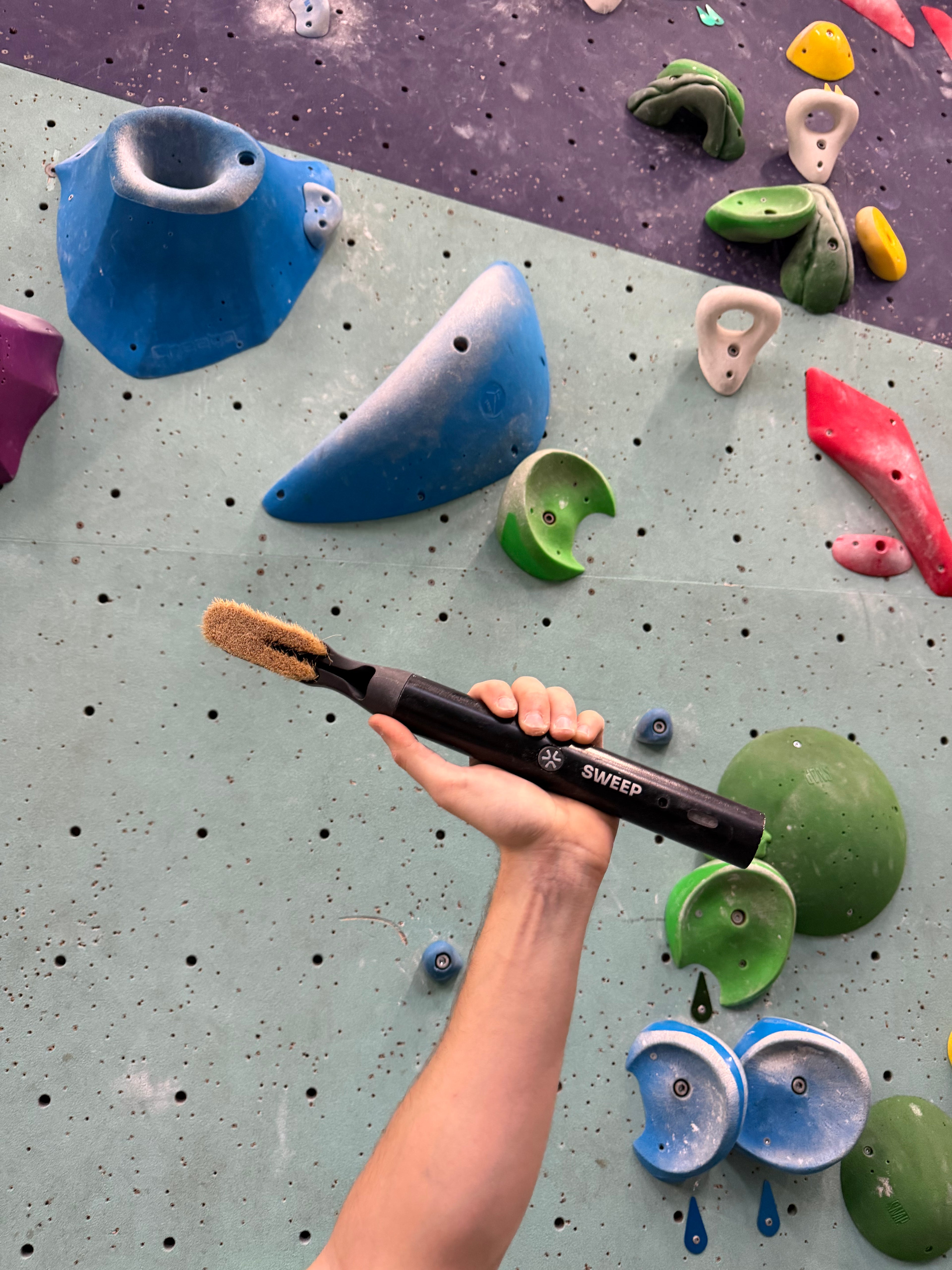 A climber holding hand high up proud with the coolest climbing brush this season called the chalk blaster. 