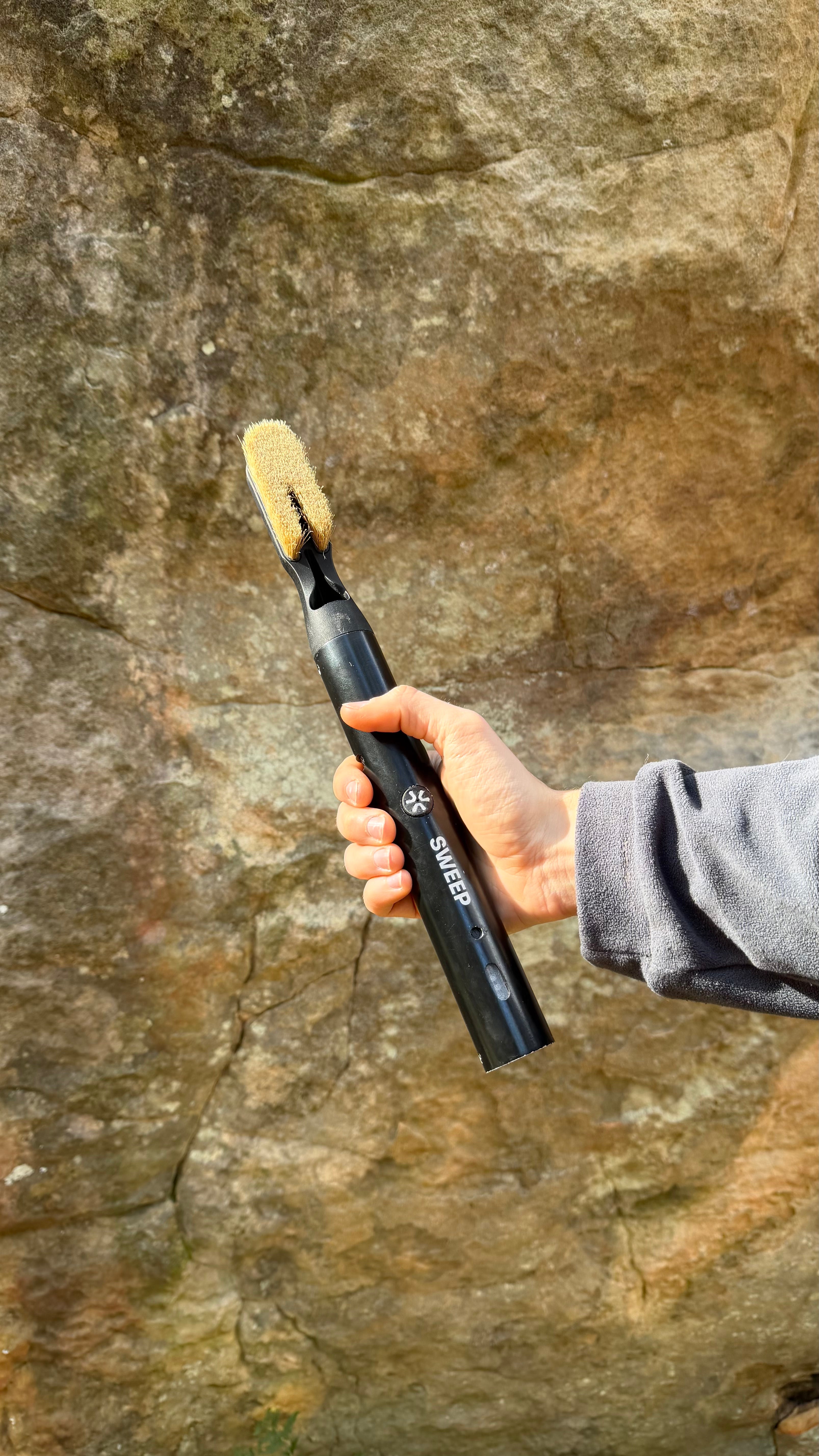 Person holding a black Chalk Blaster brush with bristles against a rocky background