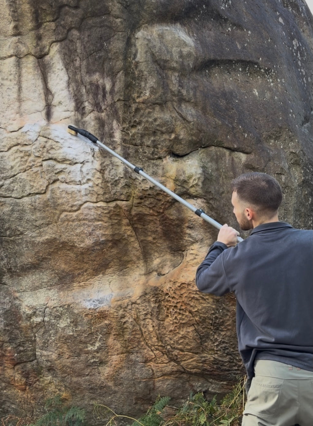 A person using the ChalkBlaster extension pole attachment to brush high to reach places. The stick brush allow the air to path through the inside and deliver directly on the climbing hold or rock.